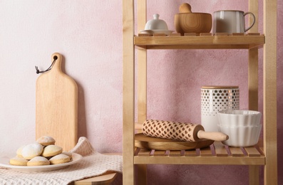 Photo of Wooden shelving unit and table with kitchenware near color wall
