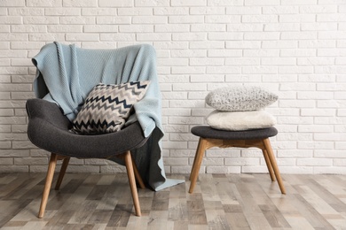 Photo of Stylish interior with plaid, pillows and armchair near brick wall