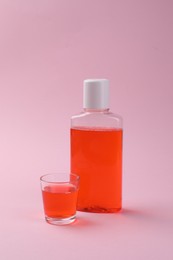 Photo of Fresh mouthwash in bottle and glass on pink background