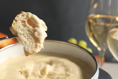 Photo of Dipping piece of bread into fondue pot with melted cheese at table, closeup