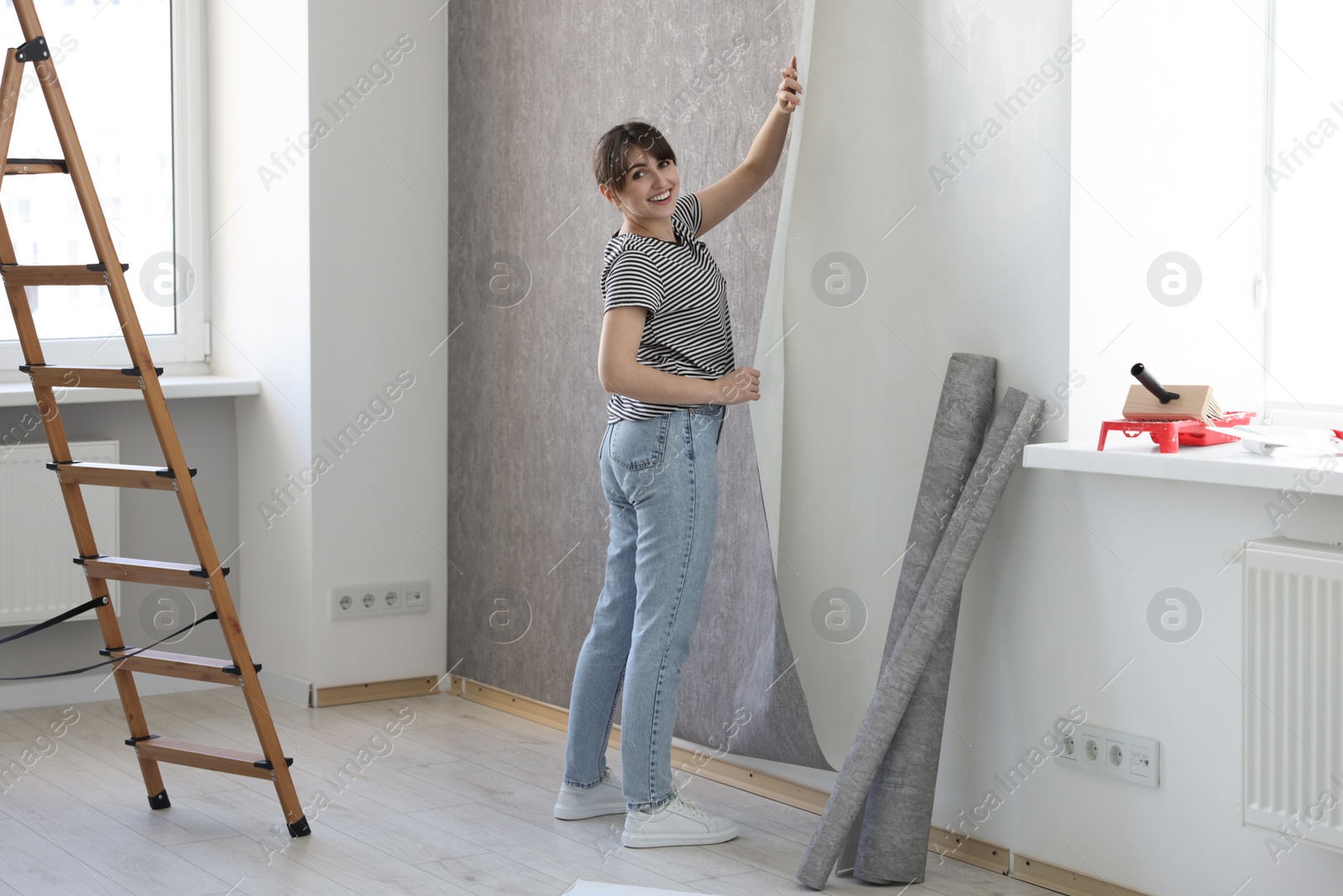 Photo of Woman hanging stylish gray wallpaper in room