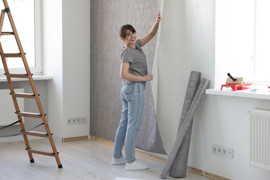 Woman hanging stylish gray wallpaper in room