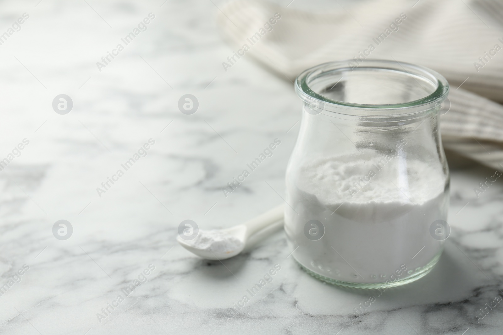 Photo of Baking powder in jar and spoon on white marble table, closeup. Space for text