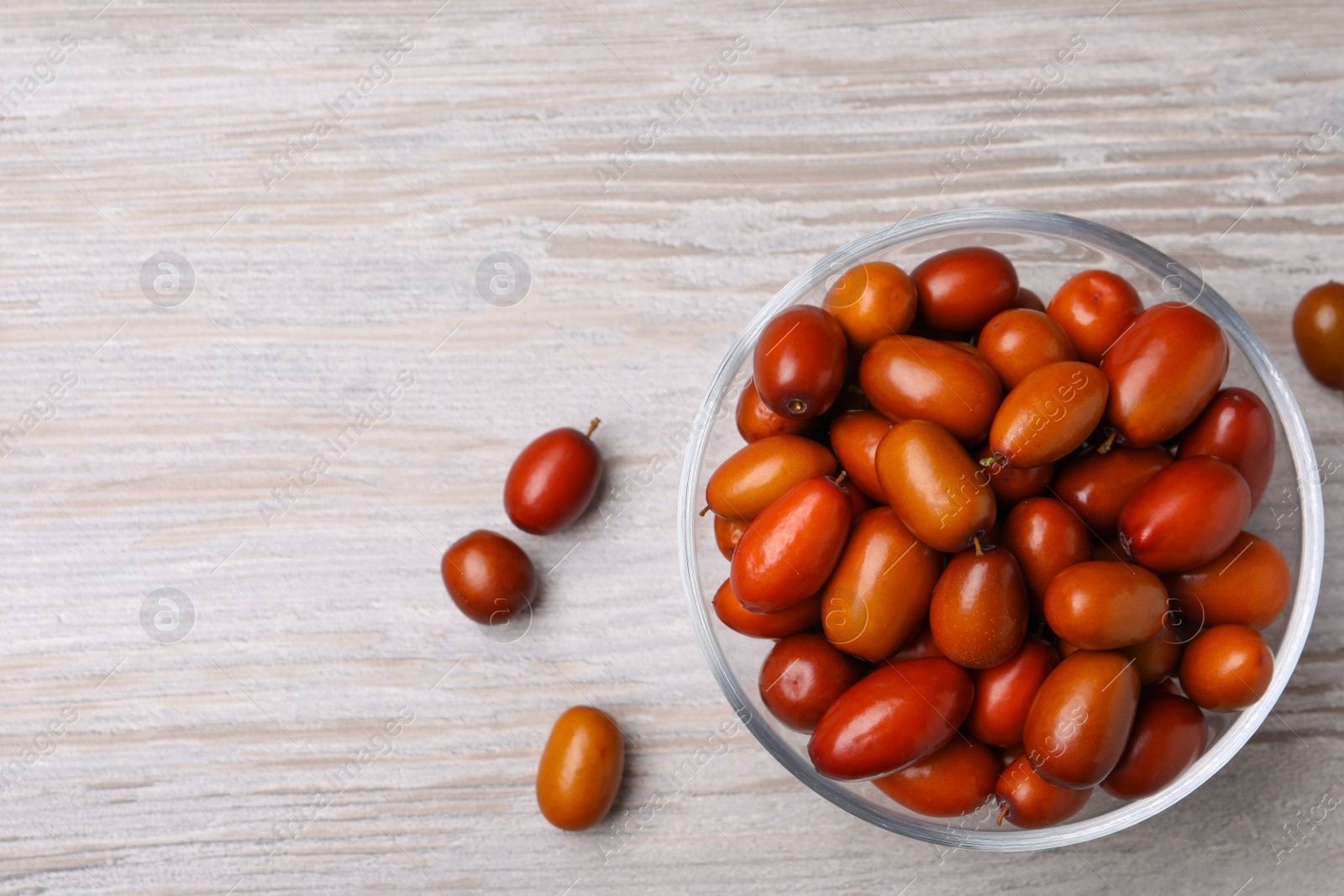 Photo of Fresh Ziziphus jujuba fruits with glass bowl on wooden table, flat lay. Space for text