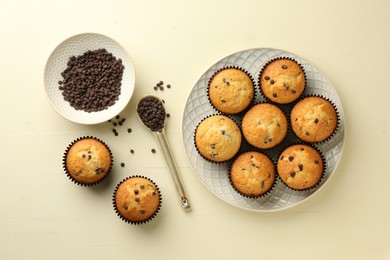 Delicious sweet muffins with chocolate chips on beige wooden table, flat lay