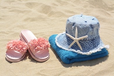 Towel with denim hat, starfish and slippers on sand outdoors. Beach accessories
