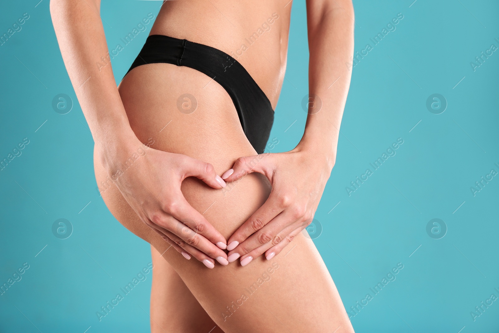 Photo of Closeup view of slim woman in underwear making heart with hands near thigh on color background. Cellulite problem concept