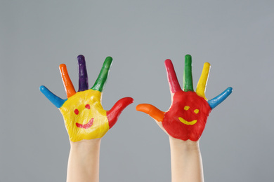 Photo of Kid with smiling faces drawn on palms against grey background, closeup