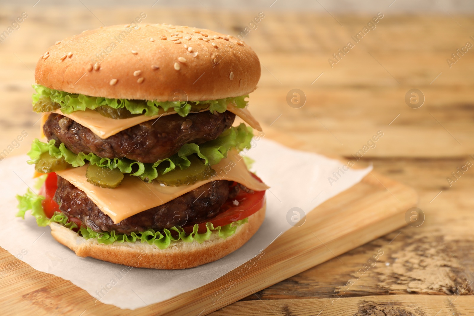 Photo of Tasty hamburger with patties on wooden table, closeup. Space for text