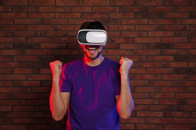 Photo of Emotional man playing video games with virtual reality headset near brick wall