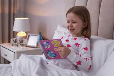 Photo of Cute little girl reading book in bed at home