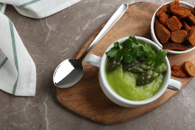 Photo of Delicious asparagus soup served on grey marble table, flat lay