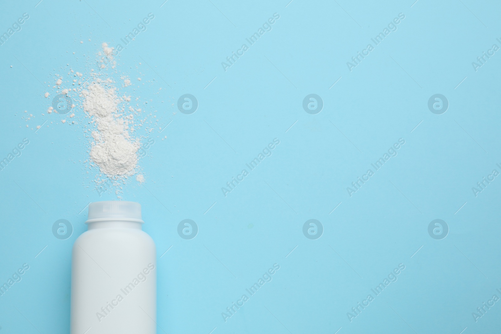 Photo of Bottle and scattered dusting powder on light blue background, top view with space for text. Baby cosmetic product