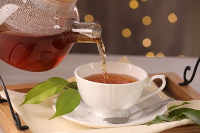 Photo of Pouring aromatic tea into cup at table, closeup