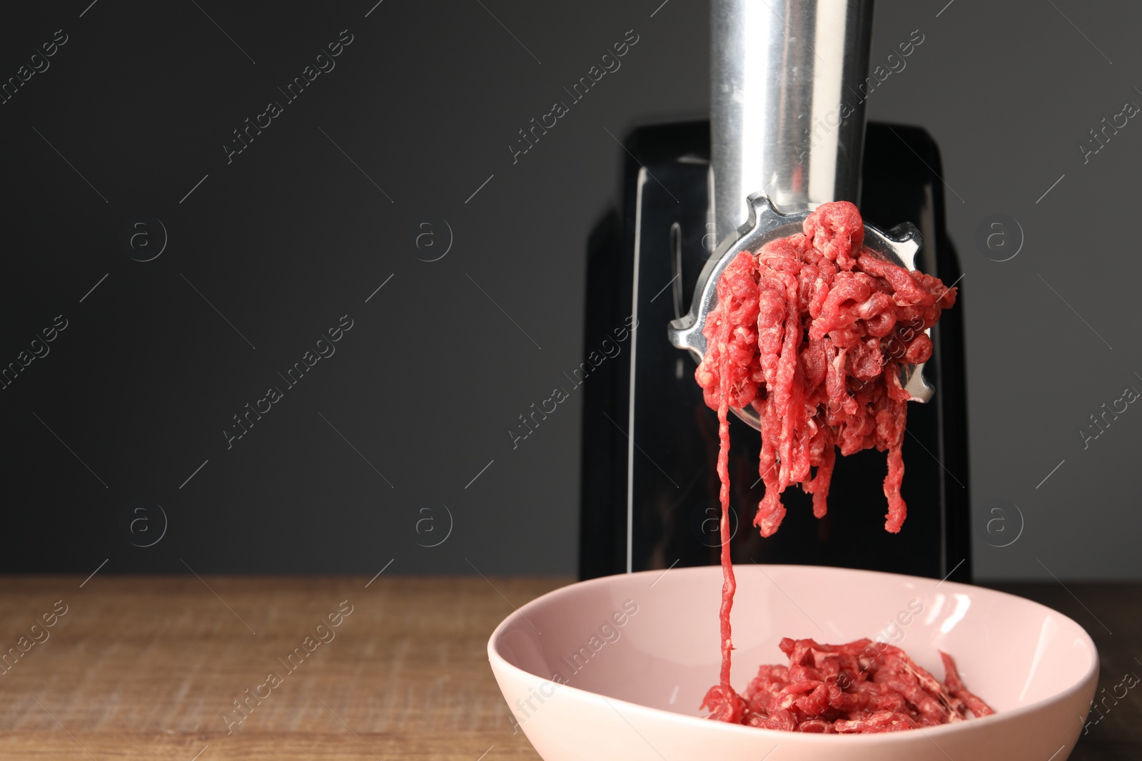 Photo of Electric meat grinder with beef mince on wooden table against grey background, closeup. Space for text