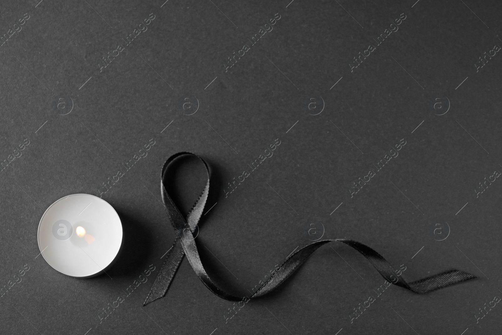 Photo of Black ribbon and burning candle on dark background, top view with space for text. Funeral symbols