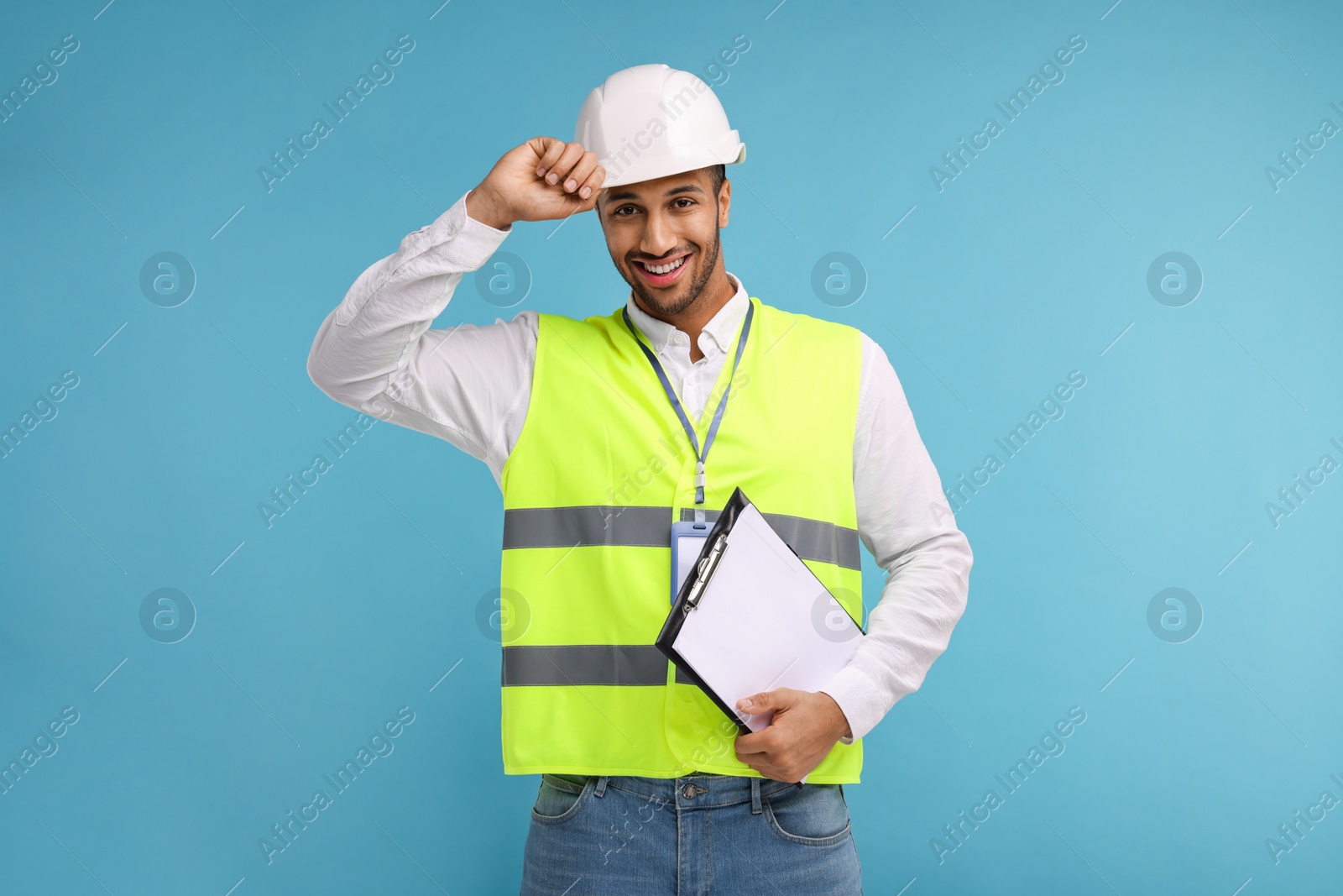 Photo of Engineer in hard hat holding clipboard on light blue background