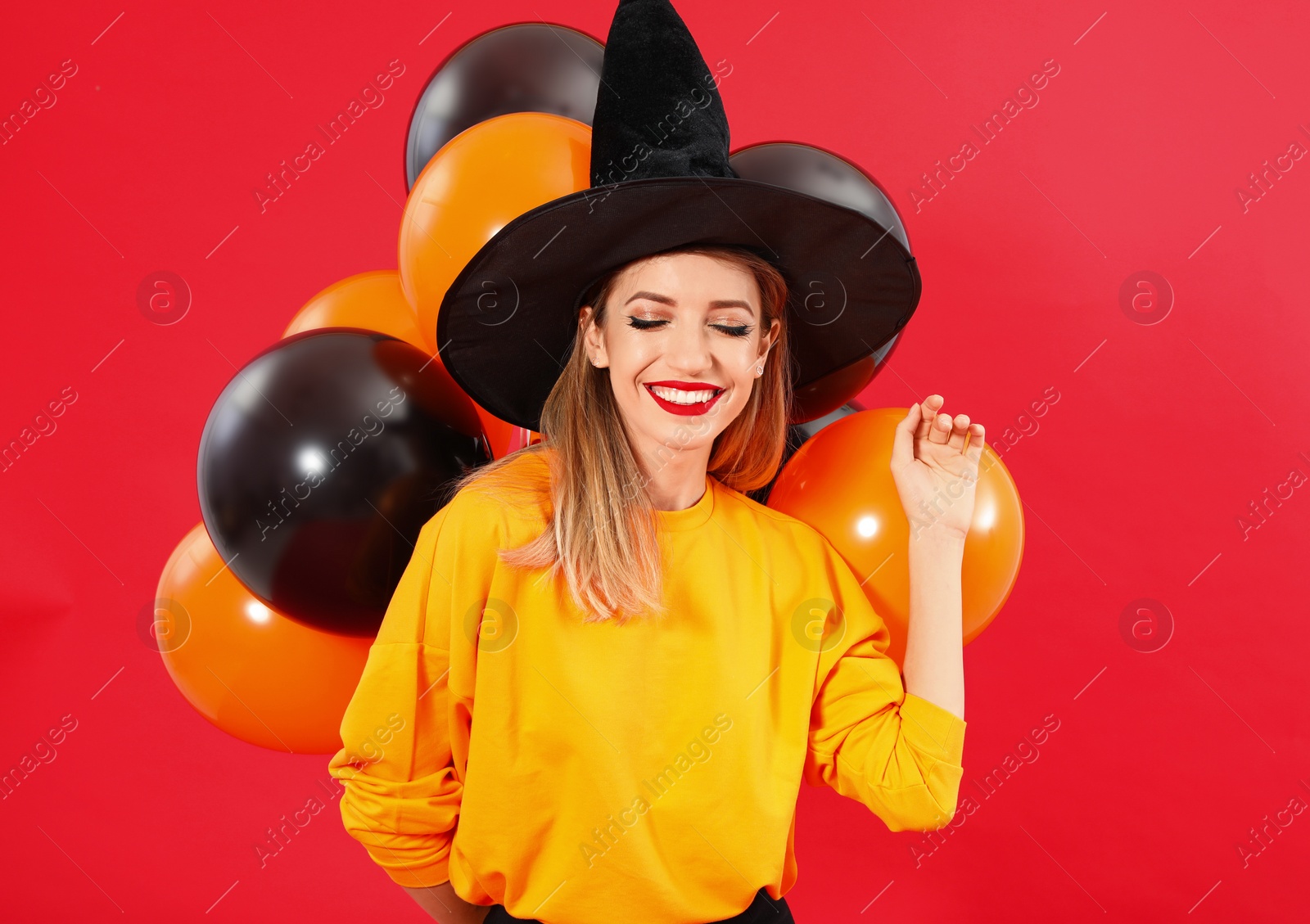 Photo of Beautiful woman wearing witch costume with balloons for Halloween party on red background