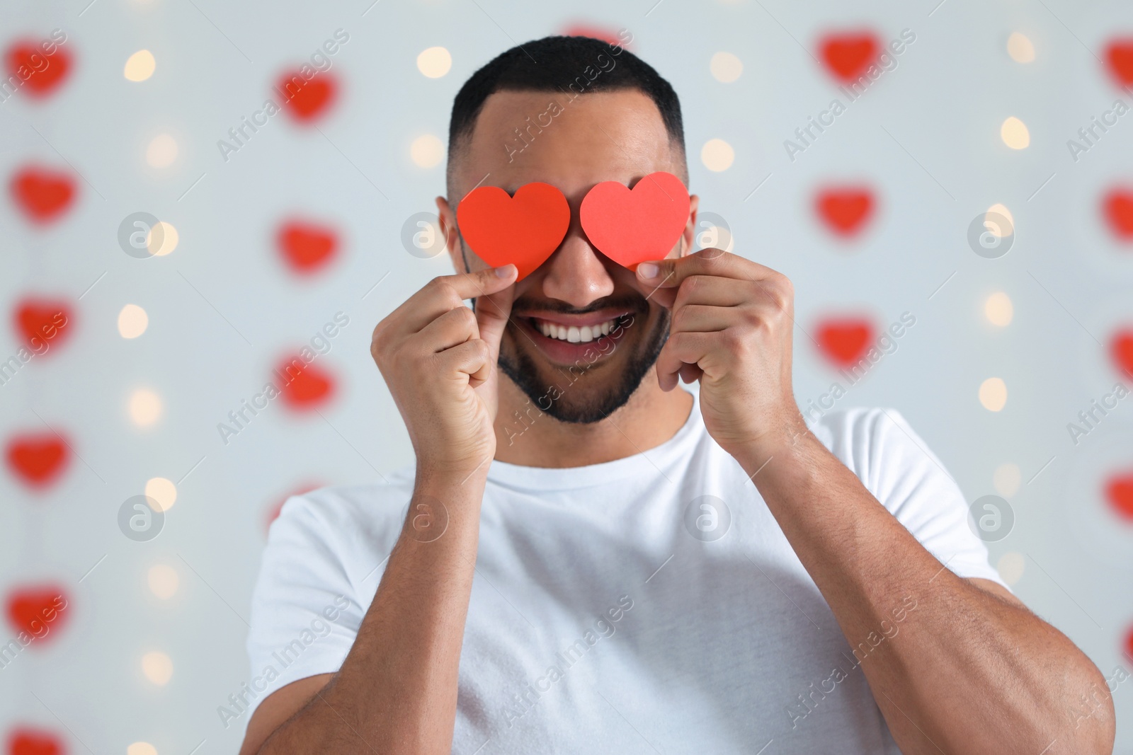 Photo of Handsome young man with red paper hearts indoors, view from camera. Valentine's day celebration in long distance relationship