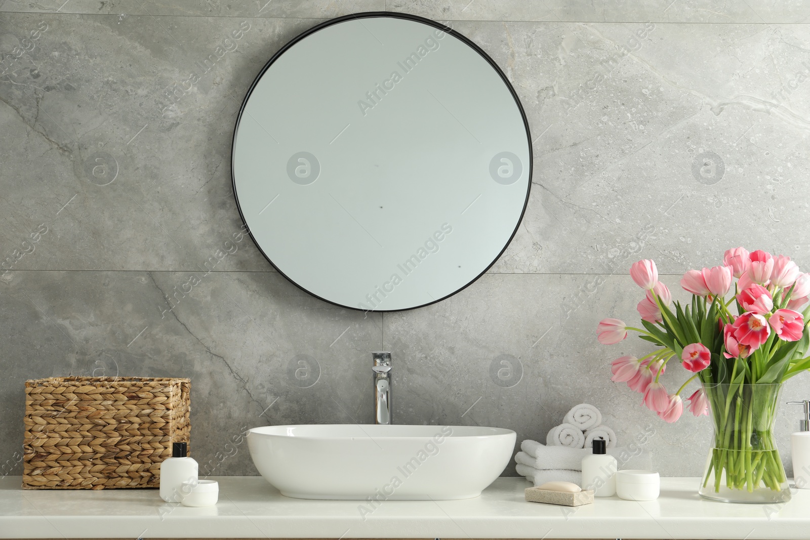 Photo of Vase with beautiful pink tulips and toiletries near sink in bathroom