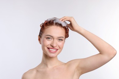 Happy young woman washing her hair with shampoo on light grey background