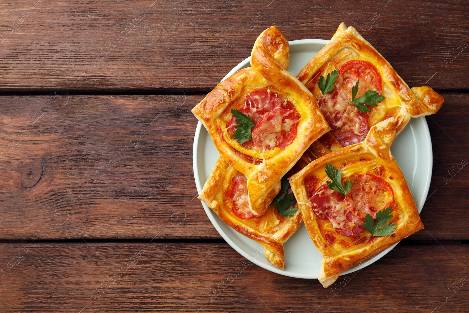 Photo of Fresh delicious puff pastry with cheese, tomatoes and parsley on wooden table, top view. Space for text