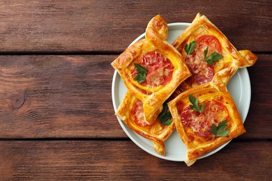 Photo of Fresh delicious puff pastry with cheese, tomatoes and parsley on wooden table, top view. Space for text