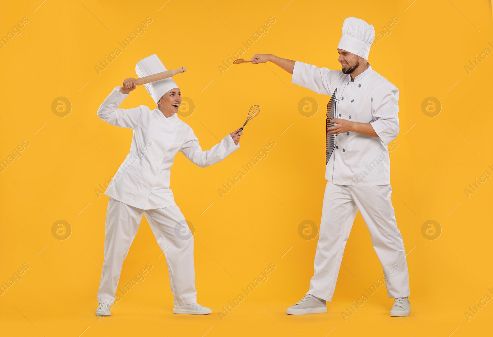 Photo of Happy professional confectioners in uniforms having fun on yellow background