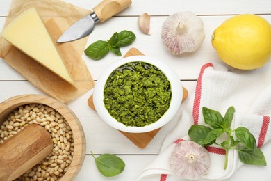 Delicious pesto sauce in bowl and ingredients on white wooden table, flat lay
