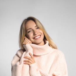 Beautiful young woman wearing knitted sweater on light grey background