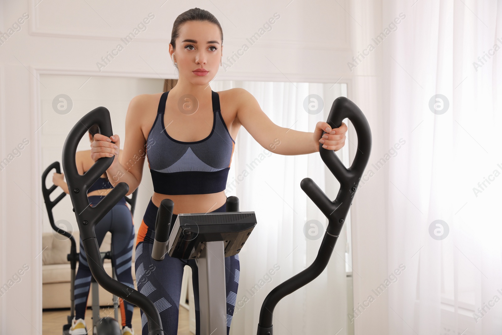 Photo of Woman using modern elliptical machine at home