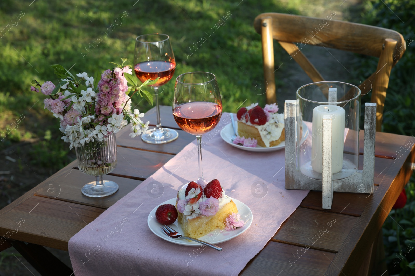 Photo of Vase with spring flowers, wine and cake on table served for romantic date in garden