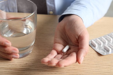 Photo of Woman with glass of water and pill at wooden table, closeup