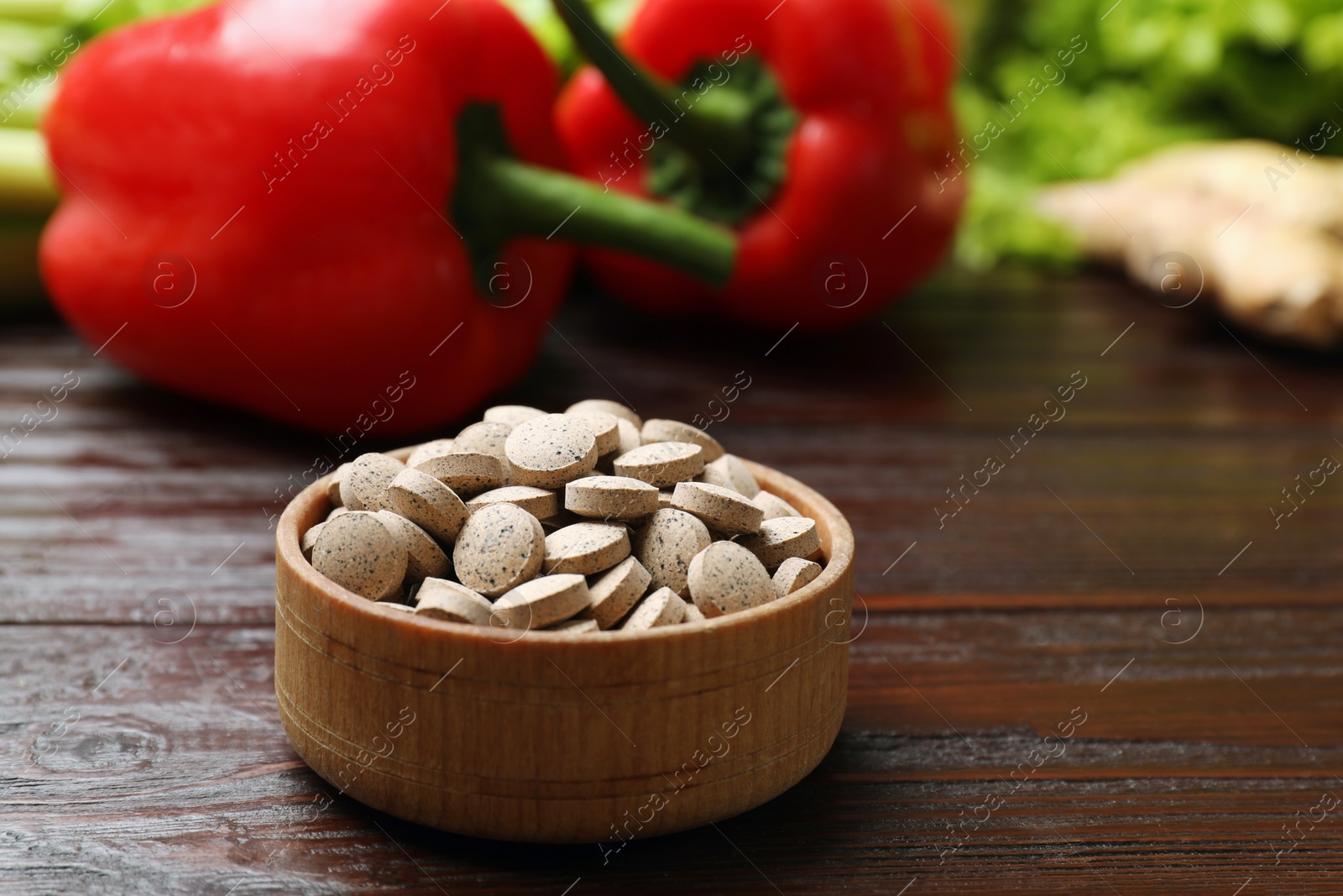 Photo of Dietary supplements. Pills in bowl and food products on wooden table, closeup