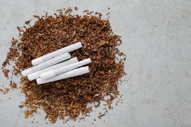 Heap of tobacco and hand rolled cigarettes on light grey table, flat lay. Space for text