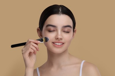 Teenage girl with makeup brush on beige background