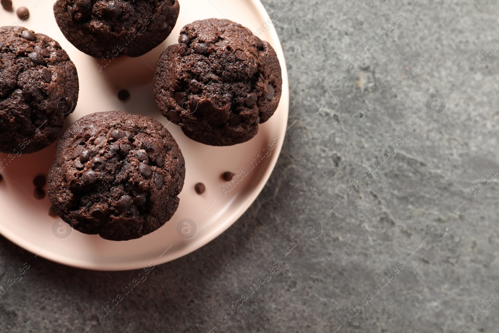 Photo of Delicious chocolate muffins on grey textured table, top view. Space for text