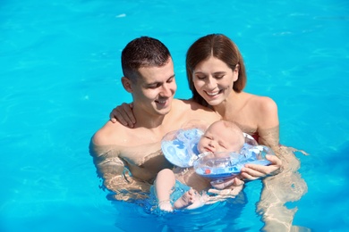 Photo of Happy parents with little baby in swimming pool on sunny day, outdoors