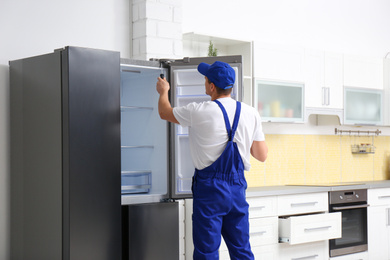 Photo of Male technician with screwdriver repairing refrigerator in kitchen