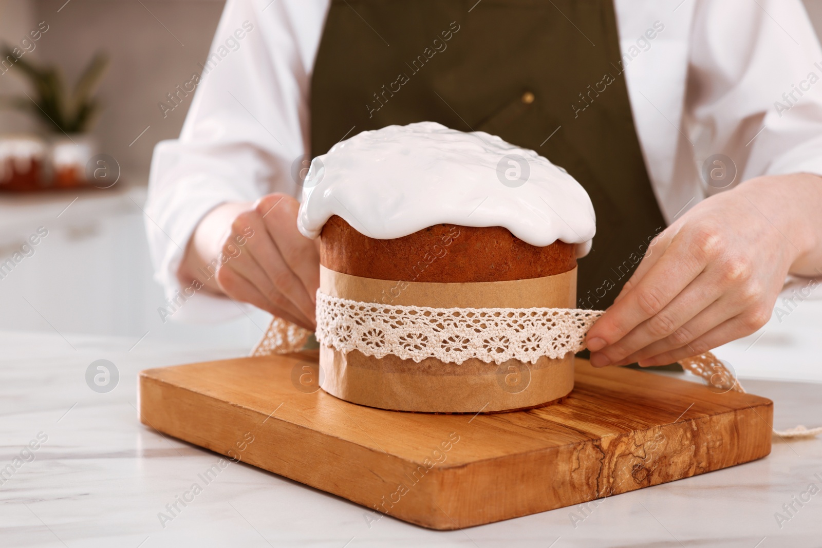 Photo of Woman wrapping delicious Easter cake with ribbon at white marble table in kitchen, closeup