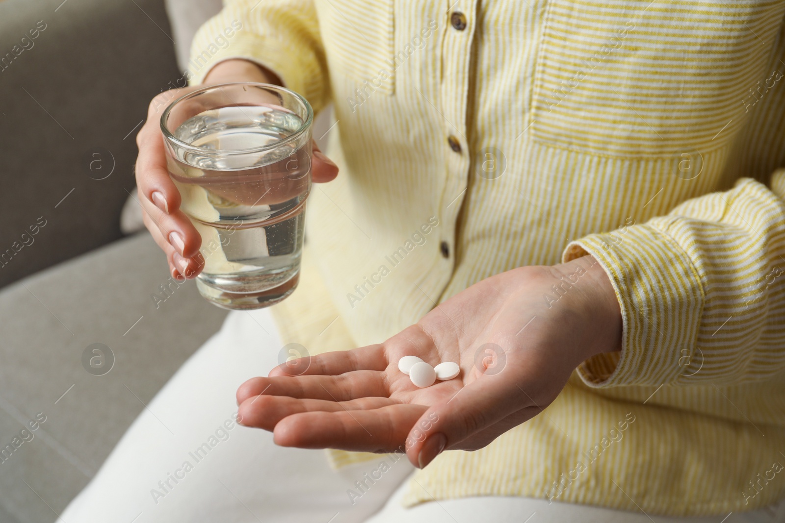 Photo of Calcium supplement. Woman holding glass of water and pills indoors, closeup