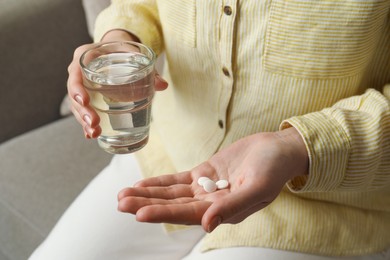 Calcium supplement. Woman holding glass of water and pills indoors, closeup