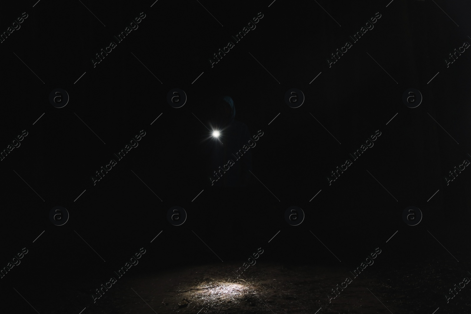 Photo of Silhouette of man with bright flashlight in forest at night