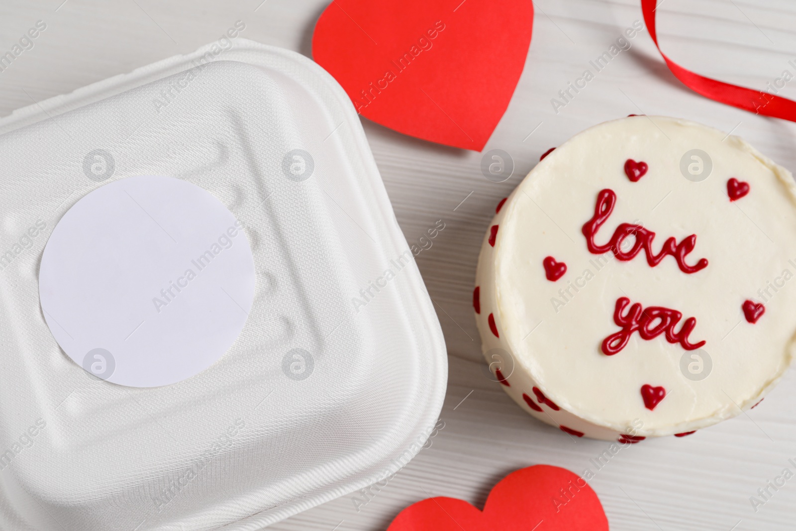 Photo of Bento cake with text Love You and takeaway packaging on white wooden table, flat lay