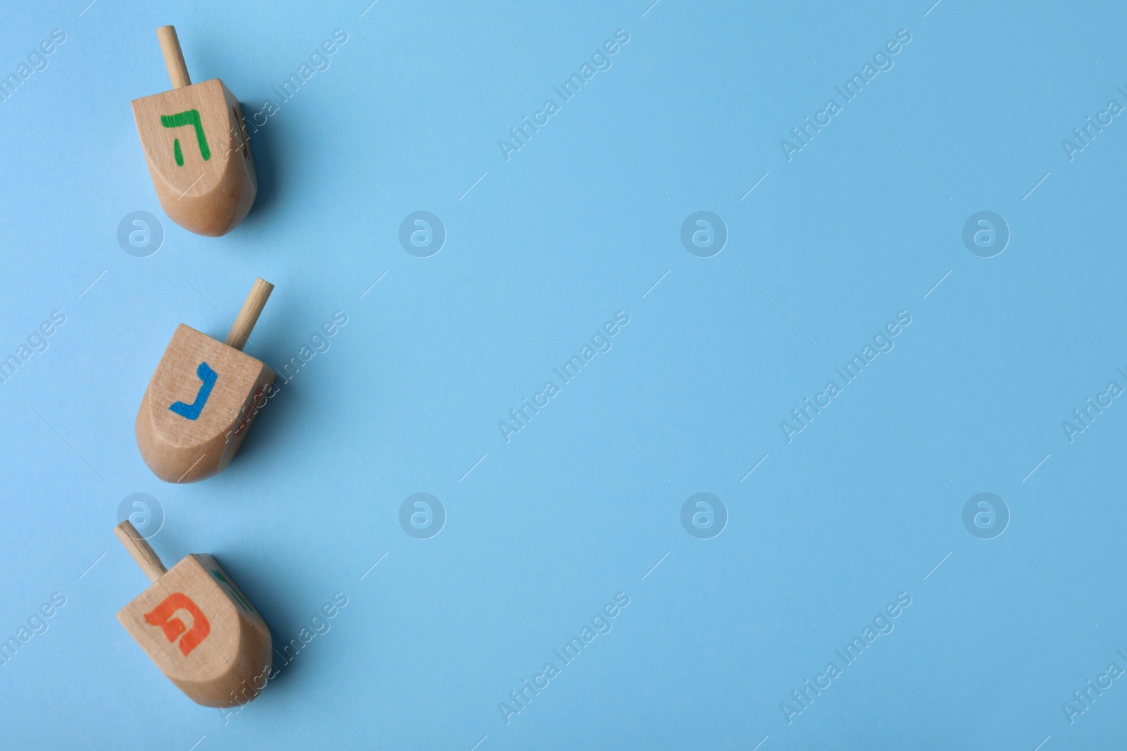 Photo of Hanukkah traditional dreidels with letters He, Pe and Nun on light blue background, flat lay. Space for text