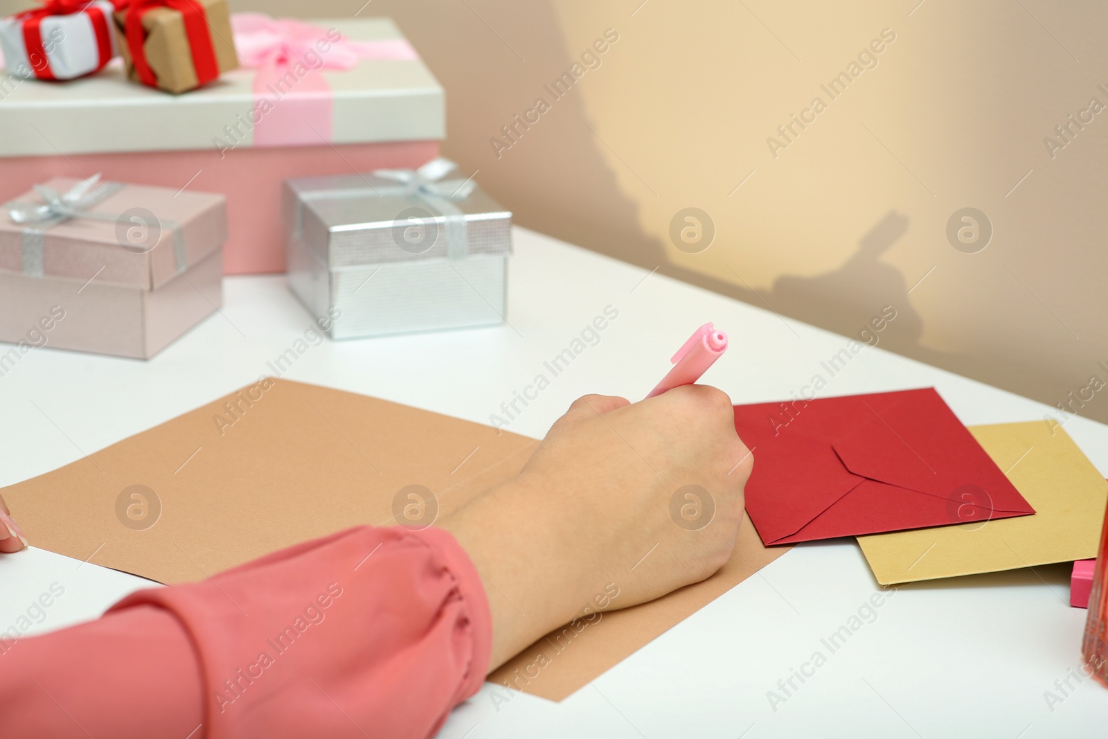 Photo of Young woman writing message in greeting card at white table, closeup