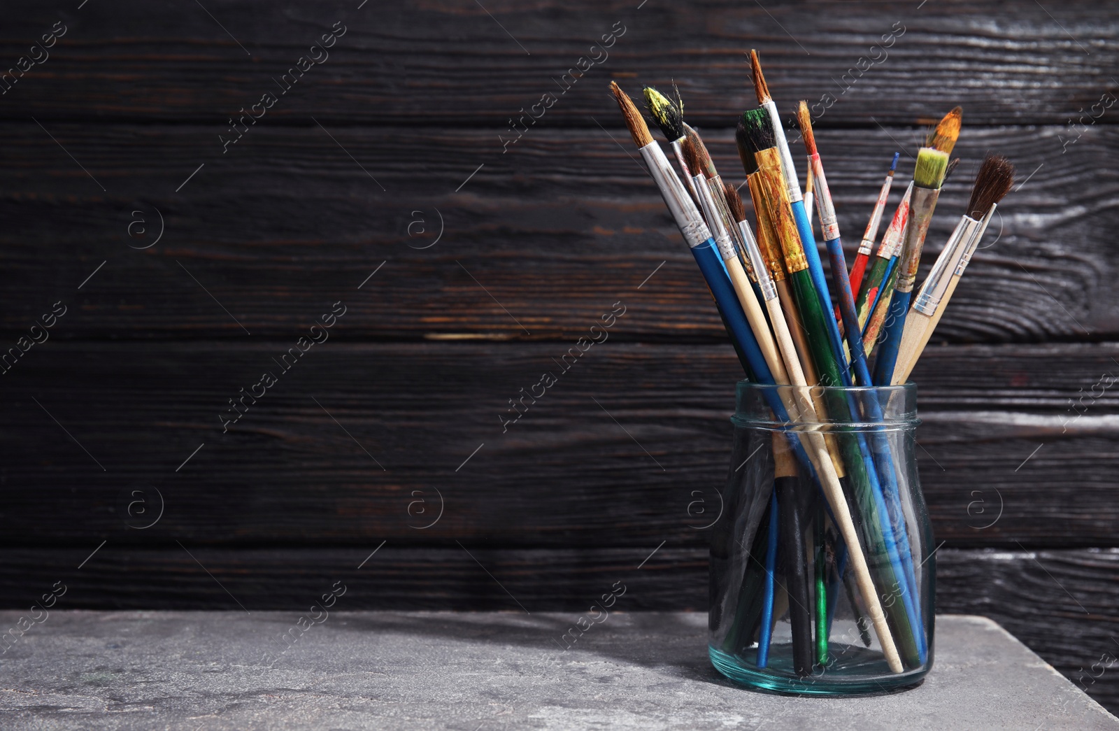 Photo of Jar with paint brushes on table against wooden background. Space for text