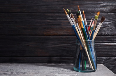 Jar with paint brushes on table against wooden background. Space for text