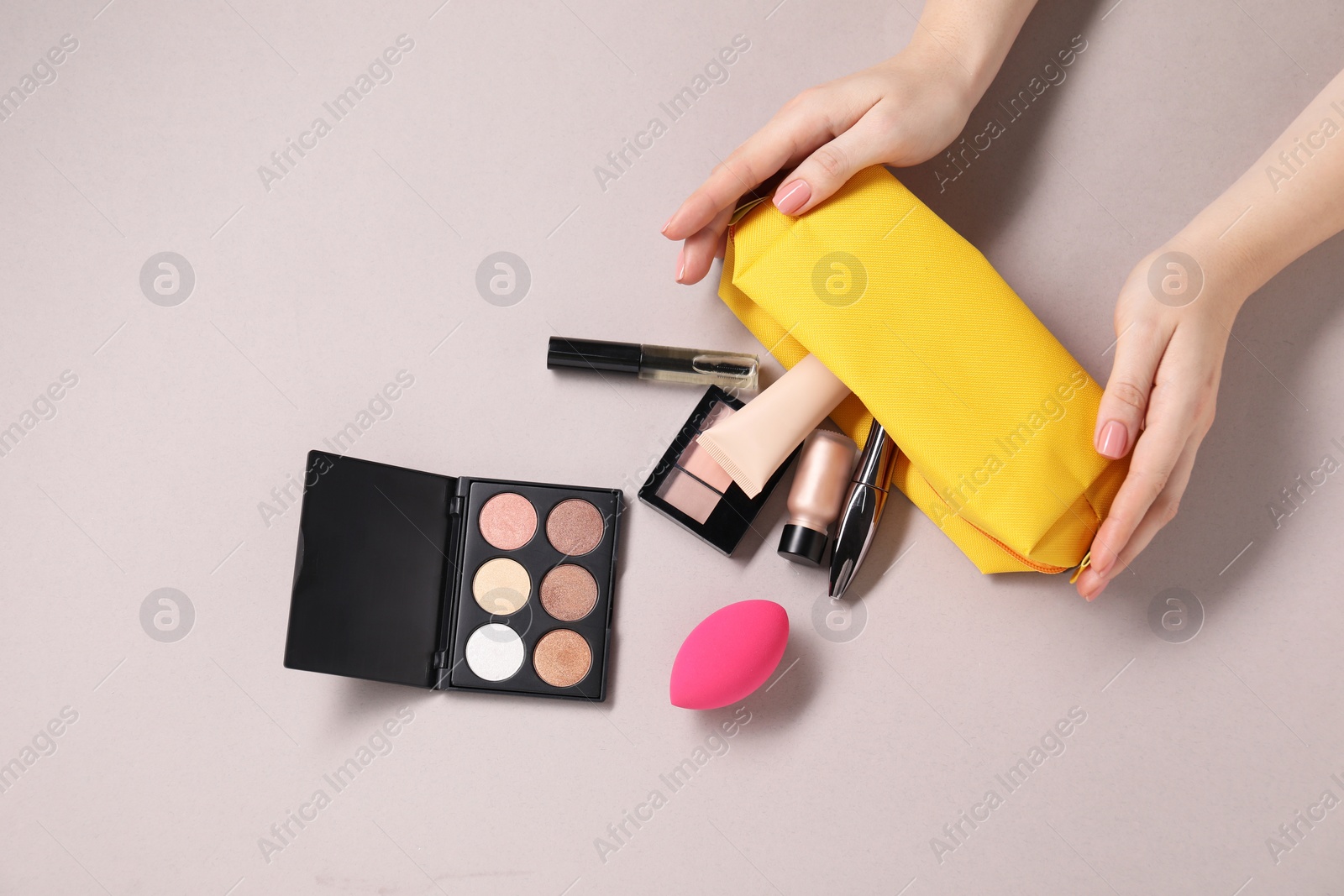 Photo of Woman with cosmetic bag and different makeup products on beige background, top view