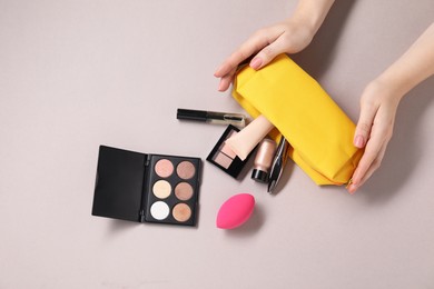 Photo of Woman with cosmetic bag and different makeup products on beige background, top view